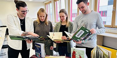 weibliche und männliche Studierenden halten Bücher in der Hand und schauen gemeinsam hinein
