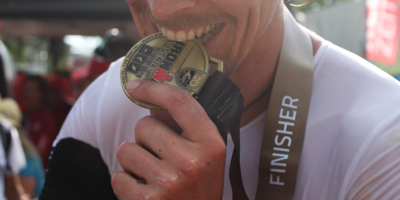 Jonas Claußen nach seinem Zieleinlauf beim Ironman 2018 andeutungsweise in die Medaille beißend