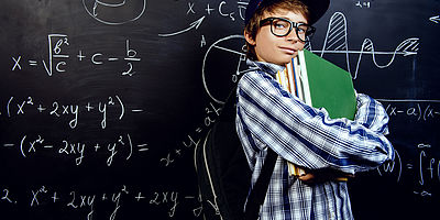 Ein Schüler steht vor einer Tafel, die mit Formeln voll geschrieben ist. Er hält Bücher in seiner Hand und lächelt selbstbewusst